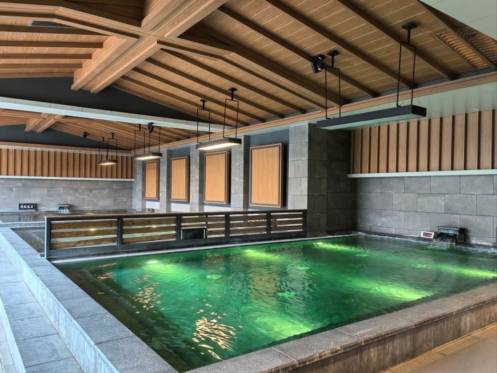 Una vasca di acqua verde, bordata di pietra, sotto un soffitto di travi di legno.